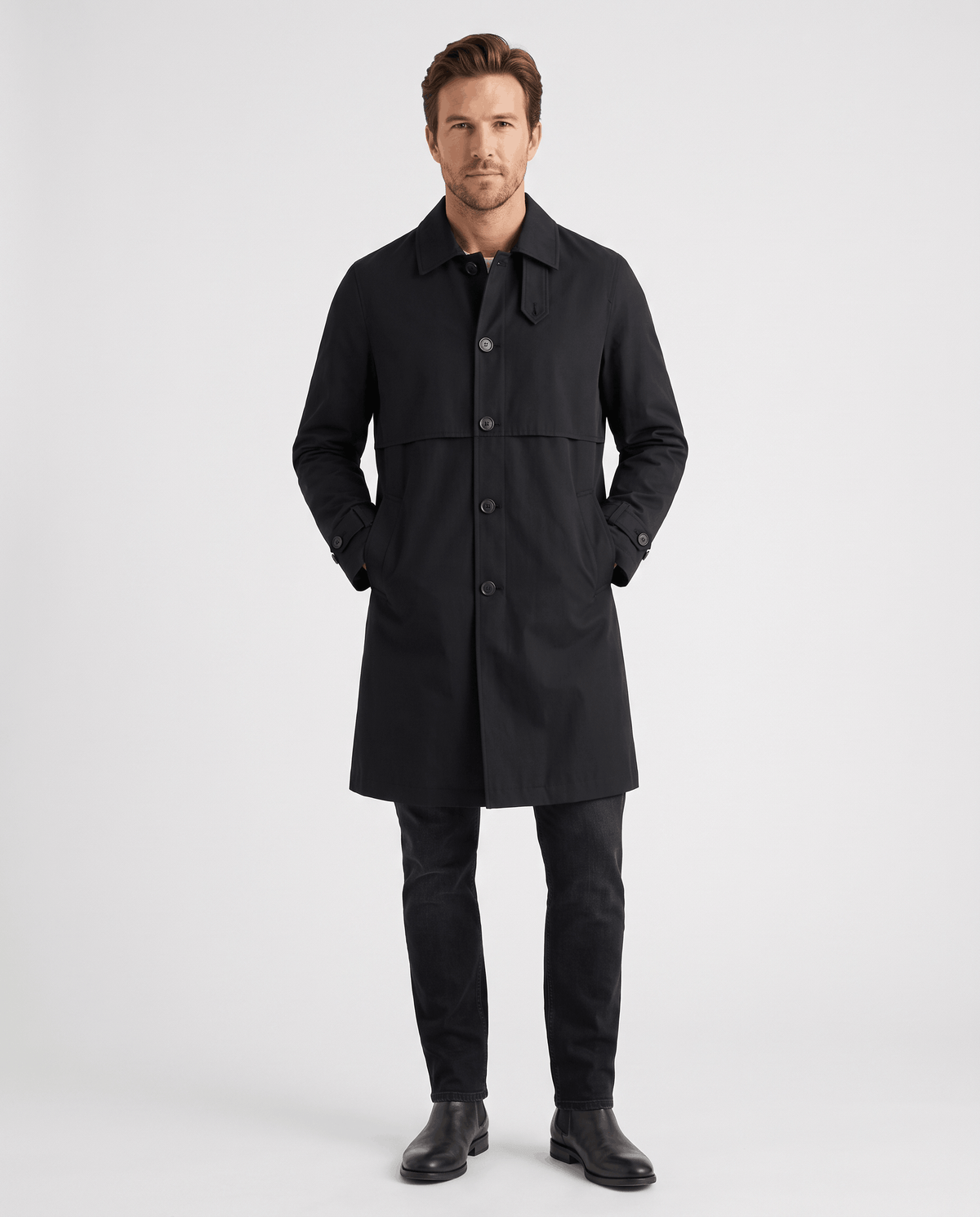 A man wearing a black mid-length single-breasted trench coat with clean lines, a button front, and an easy layering fit