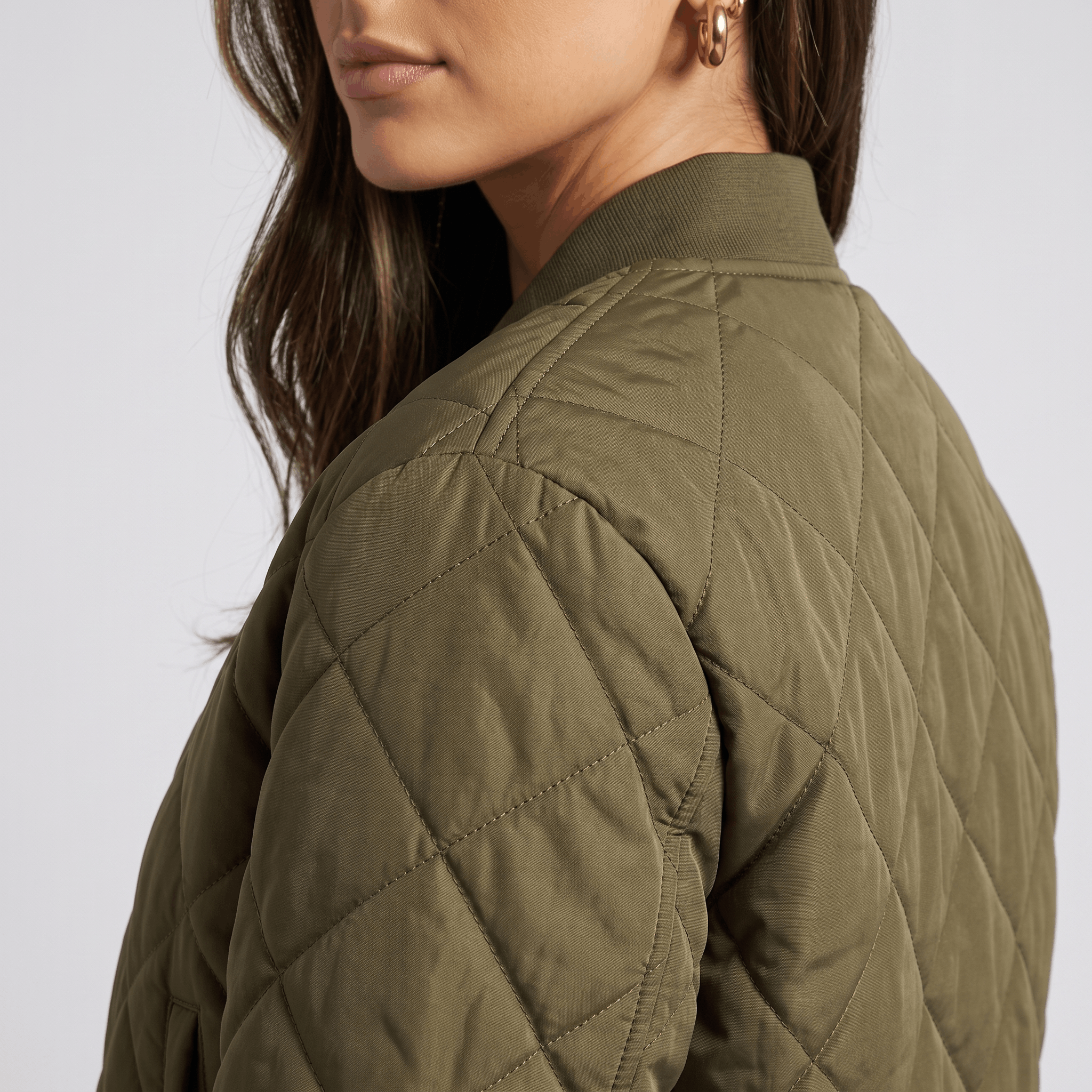 Side view of an olive green quilted jacket, highlighting the diamond-stitched texture and shoulder.