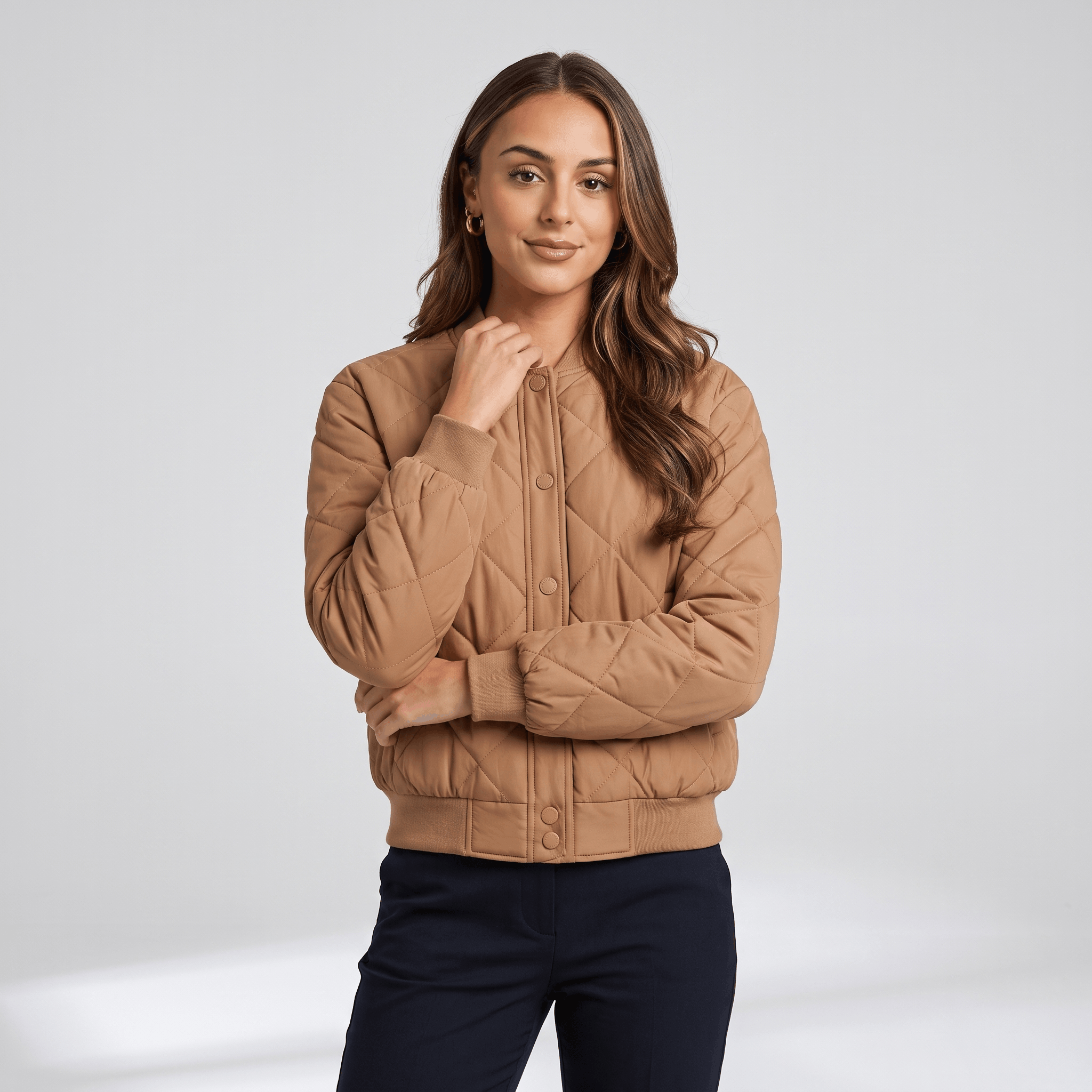 Female model wearing the tan quilted jacket with dark trousers, standing with her arms crossed.