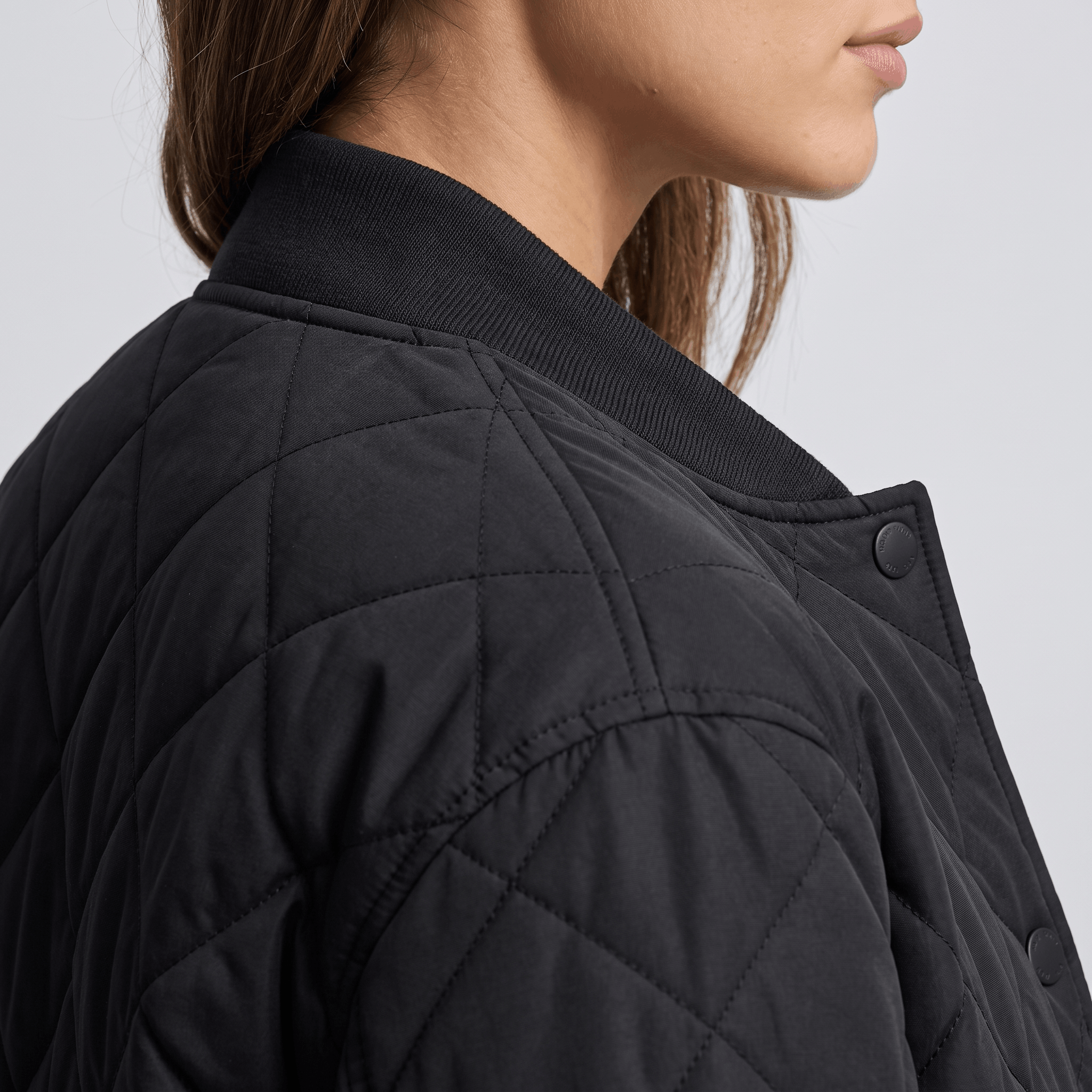 Detailed view of the black quilted jacket, highlighting the diamond quilting, collar, and snap-button closure.