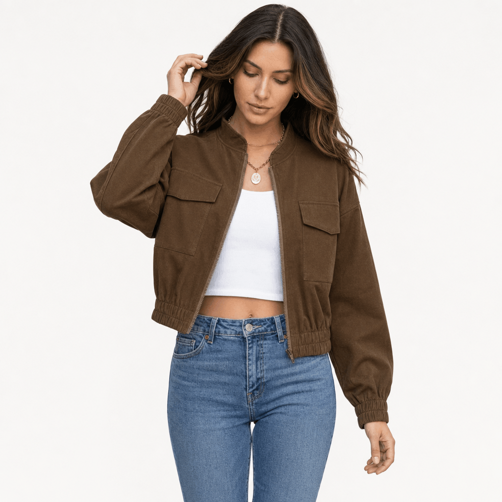 Female model wearing a brown cropped utility jacket with a stand collar and buttoned chest pockets, paired with a white crop top and blue jeans.