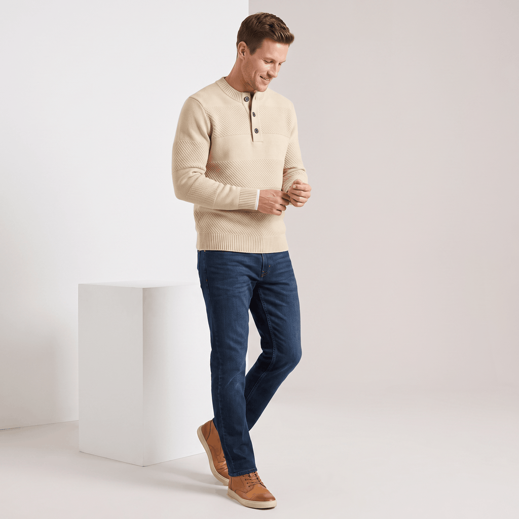 Beige chunky knit henley sweater with textured stripes, three-button placket, and ribbed trim worn with dark blue jeans.