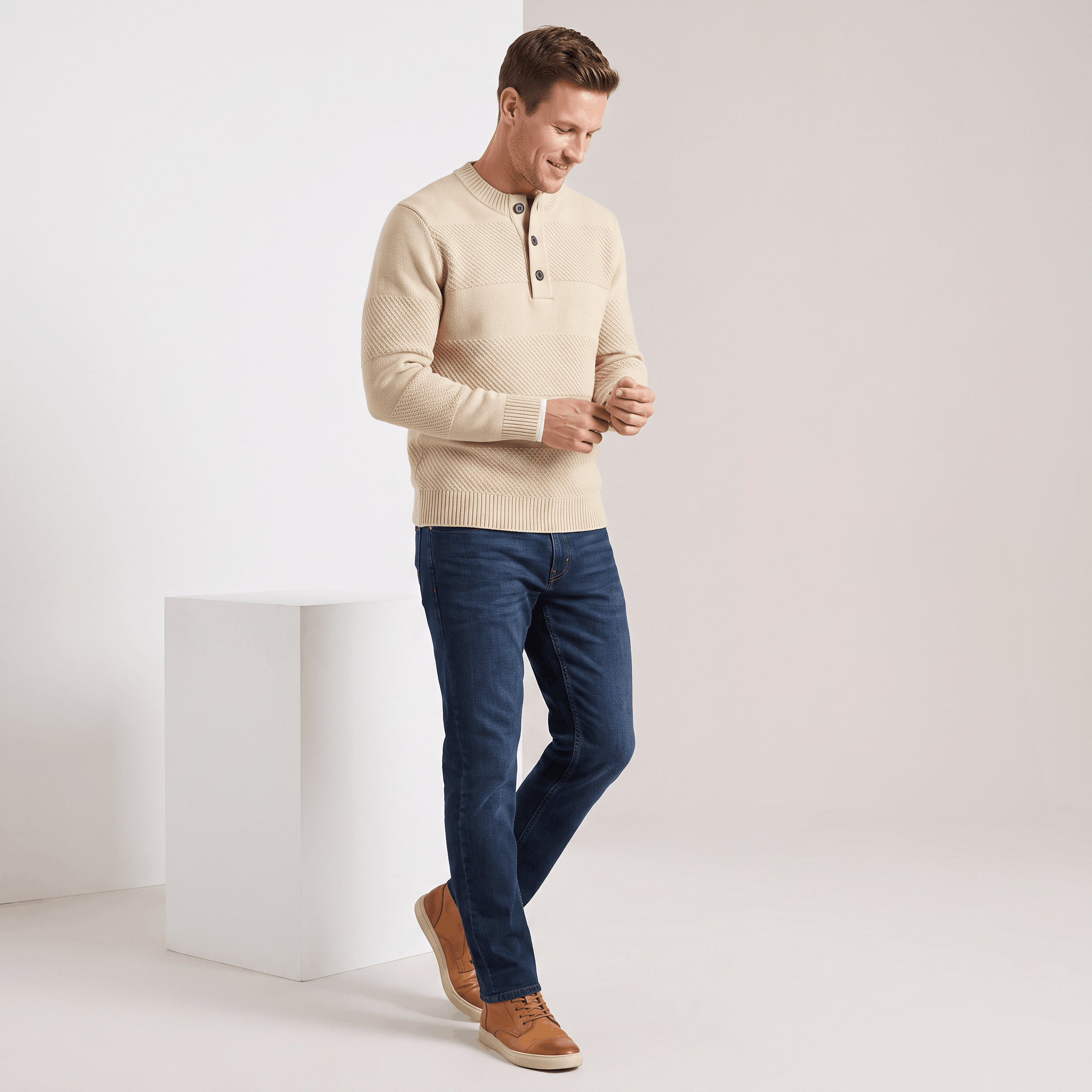 Beige chunky knit henley sweater with textured stripes, three-button placket, and ribbed trim worn with dark blue jeans.