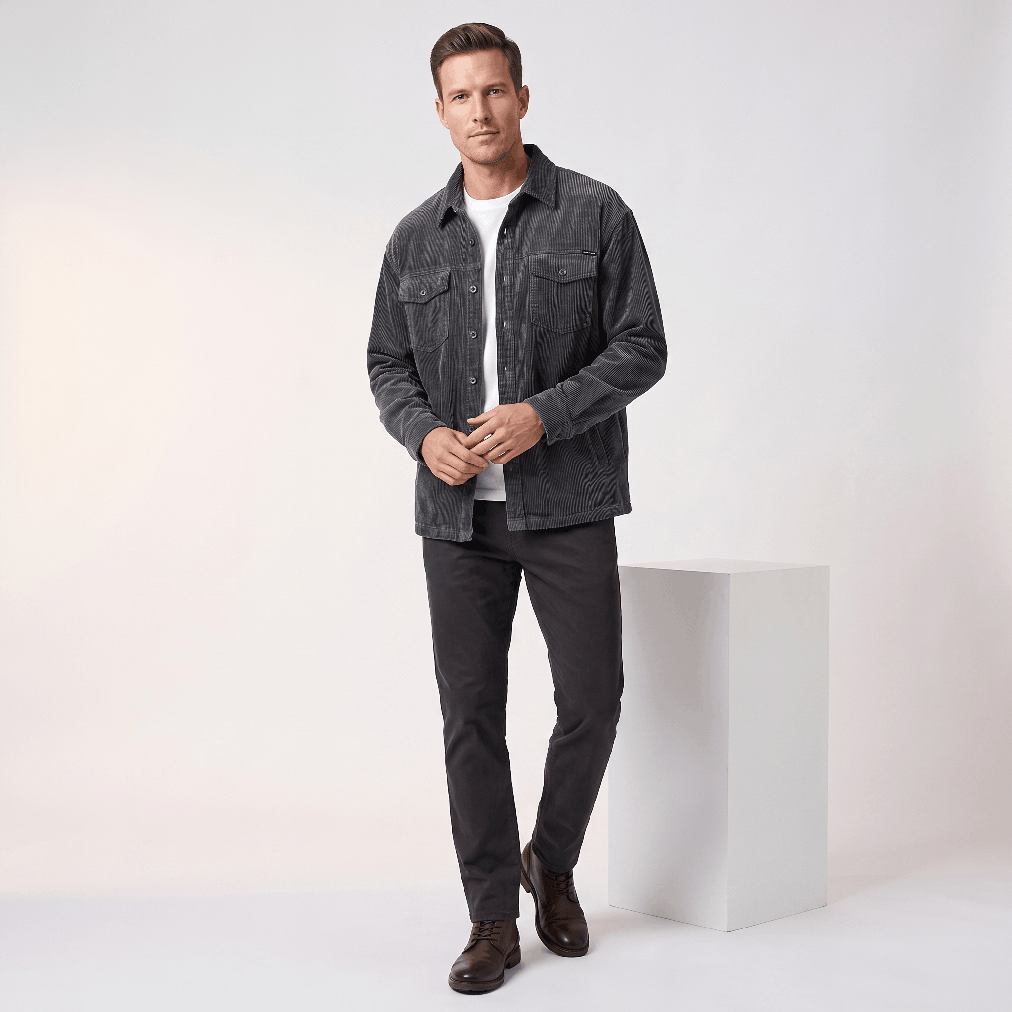 Charcoal grey corduroy shirt jacket with four pockets and antiqued buttons, worn over a white tee in a relaxed fit.