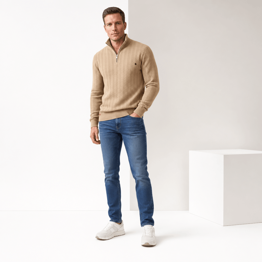 Full-body view of a man wearing a beige textured half-zip sweater with blue jeans.