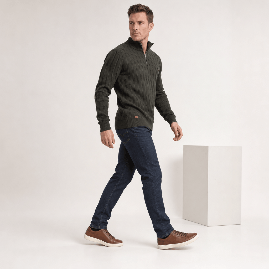 Full-body side view of the man wearing the dark olive green textured half-zip sweater with dark pants.
