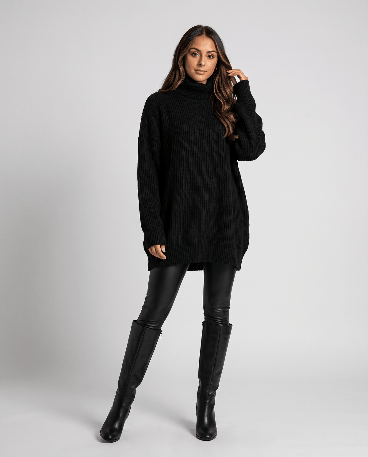 Black Oversized Longline Sweater worn by a female model with black leggings and boots, showcasing the relaxed slouchy fit, high turtleneck collar, long sleeves, and longline silhouette.