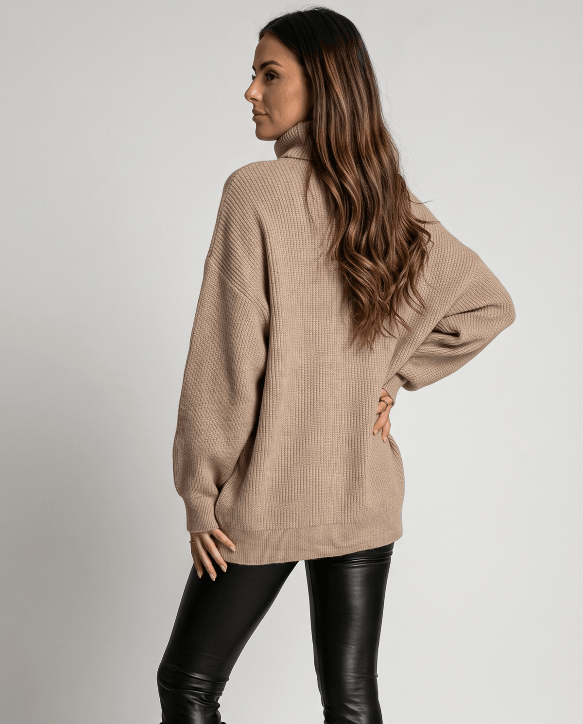 Beige Oversized Longline Sweater worn by a female model, shown from the side with a relaxed fit, high turtleneck collar, long sleeves, and extended hem.