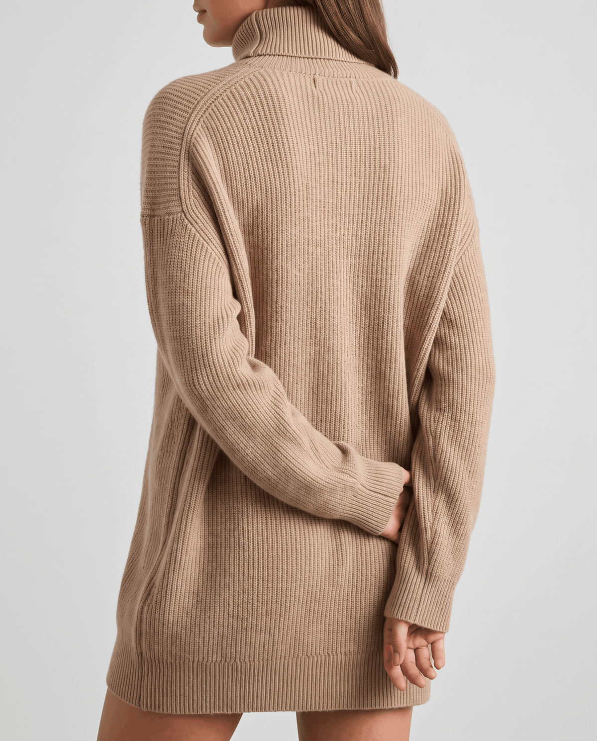 Beige Oversized Longline Sweater worn by a female model from the back, showcasing the slouchy oversized fit, high turtleneck collar, soft knit texture, and extended hem.