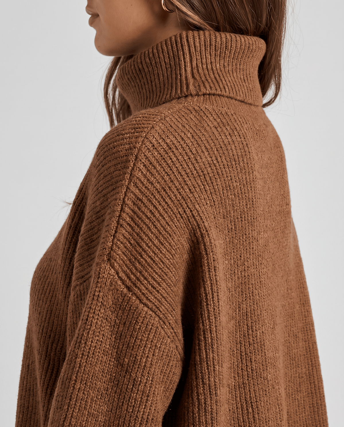 Close-up of the brown Oversized Longline Sweater worn by a female model, highlighting the high turtleneck collar, soft knit texture, and relaxed fit.