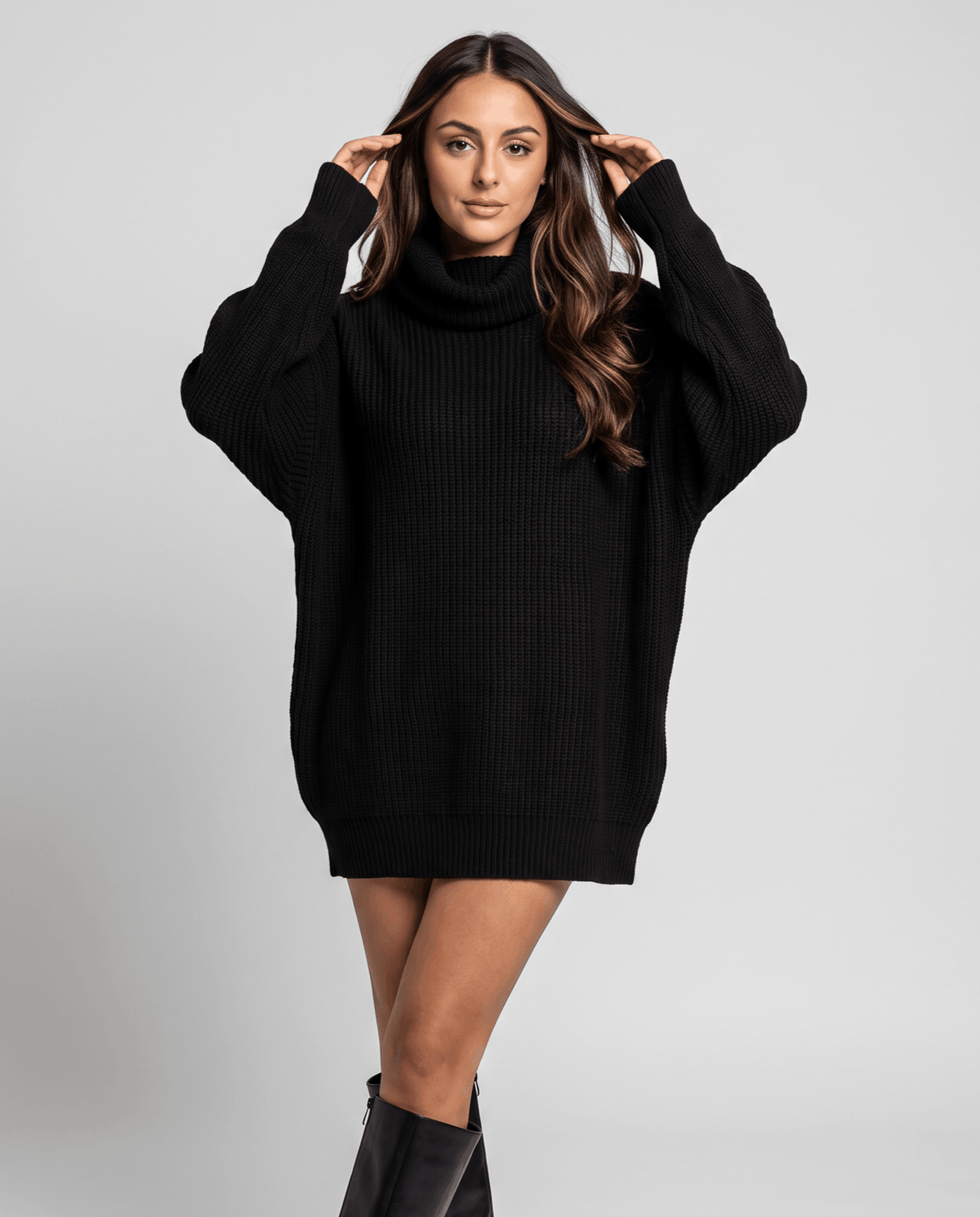 Black Oversized Longline Sweater worn by a female model with a short skirt and boots, featuring a slouchy fit, high turtleneck collar, long sleeves, and soft knit texture.