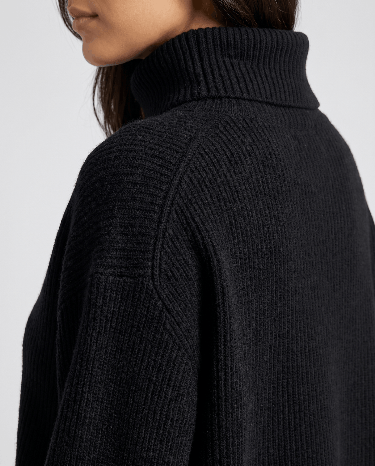 Close-up of the black Oversized Longline Sweater worn by a female model, highlighting the high turtleneck collar and soft knit texture.