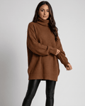 Brown Oversized Longline Sweater worn by a female model, featuring a slouchy fit, soft knit texture, high turtleneck collar, long sleeves, and extended hem.