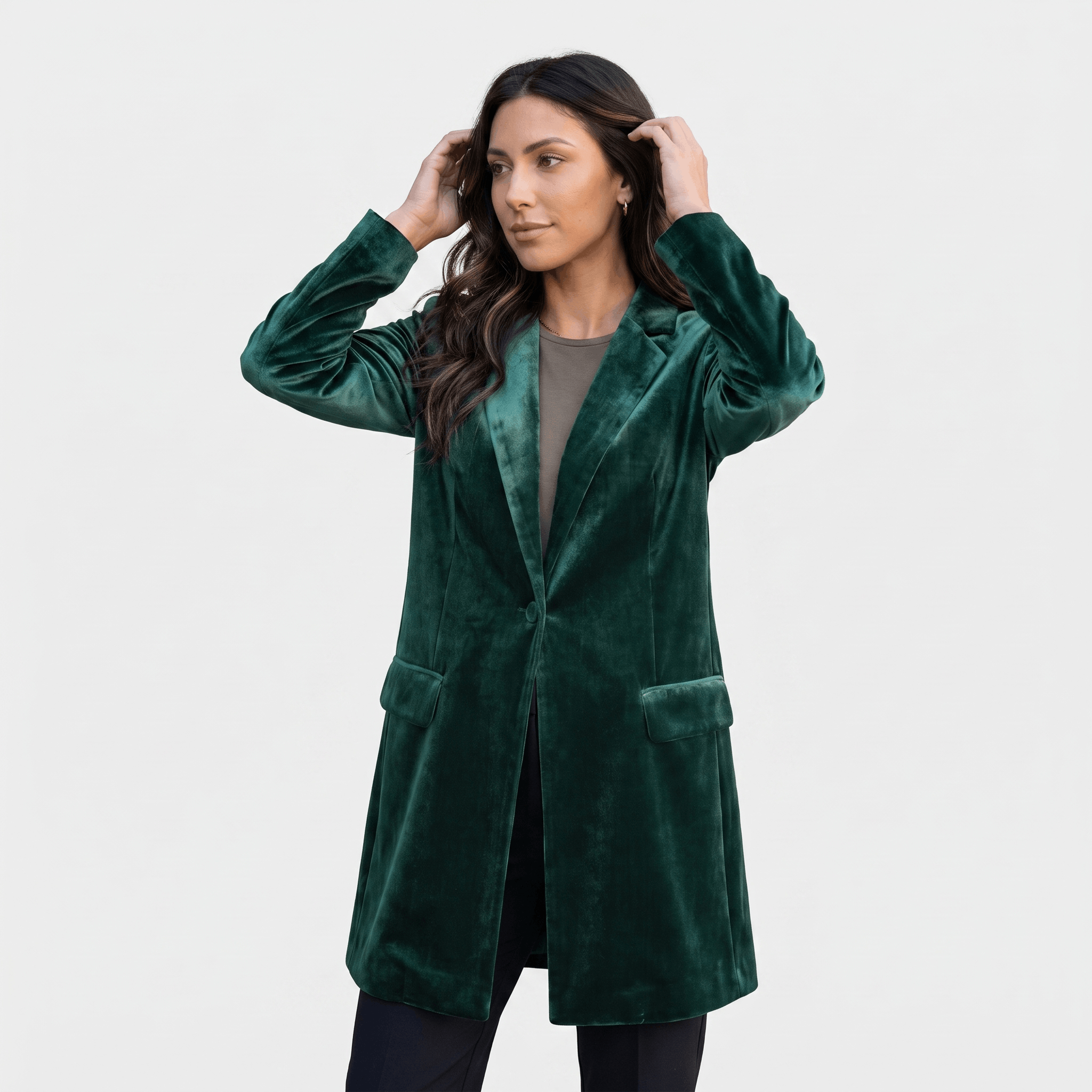 Female model wearing a dark green velvet long blazer coat with a notched lapel and long sleeves.