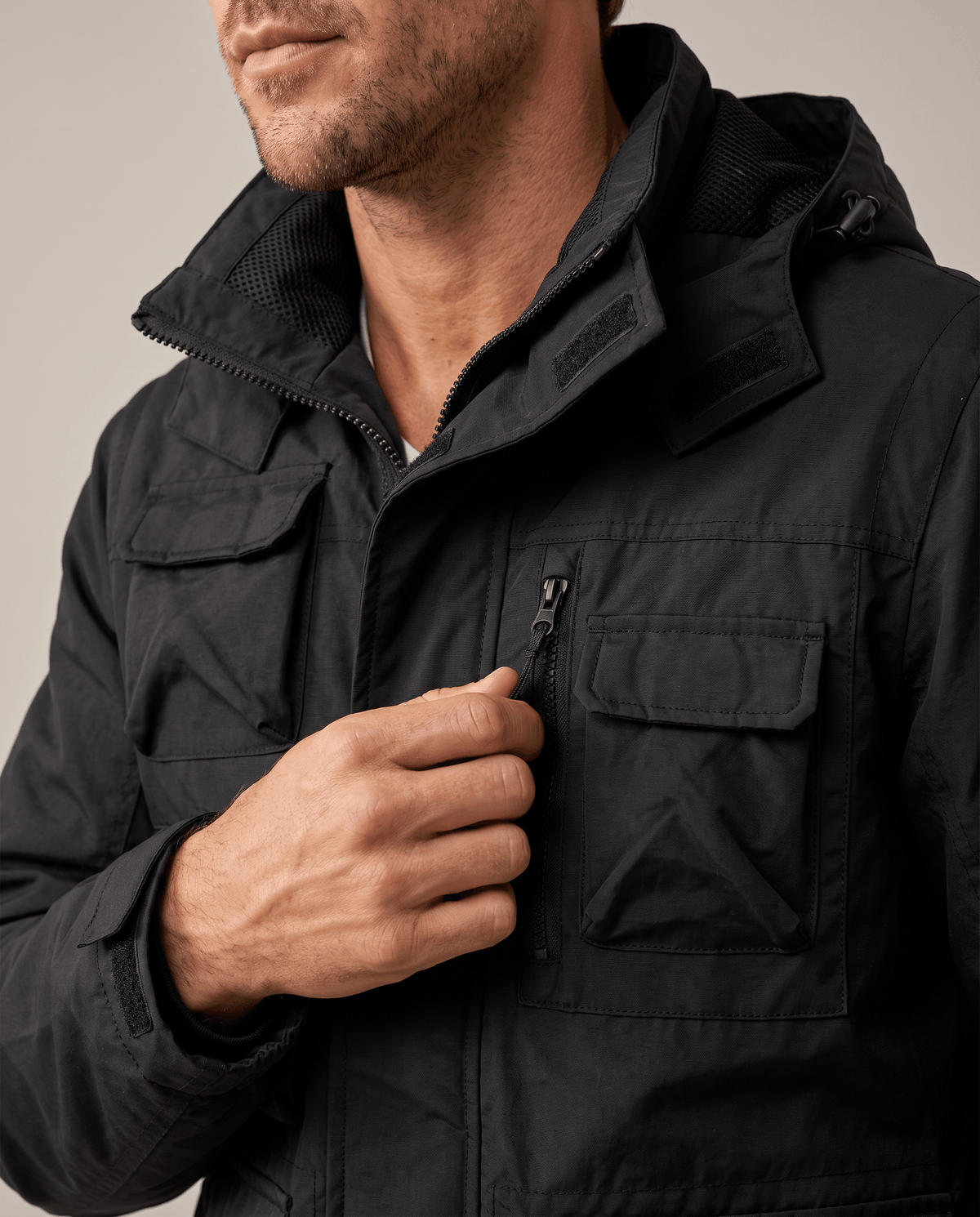 Close-up of a man wearing a black parka jacket, showing the hood, padded lining, and front pocket details