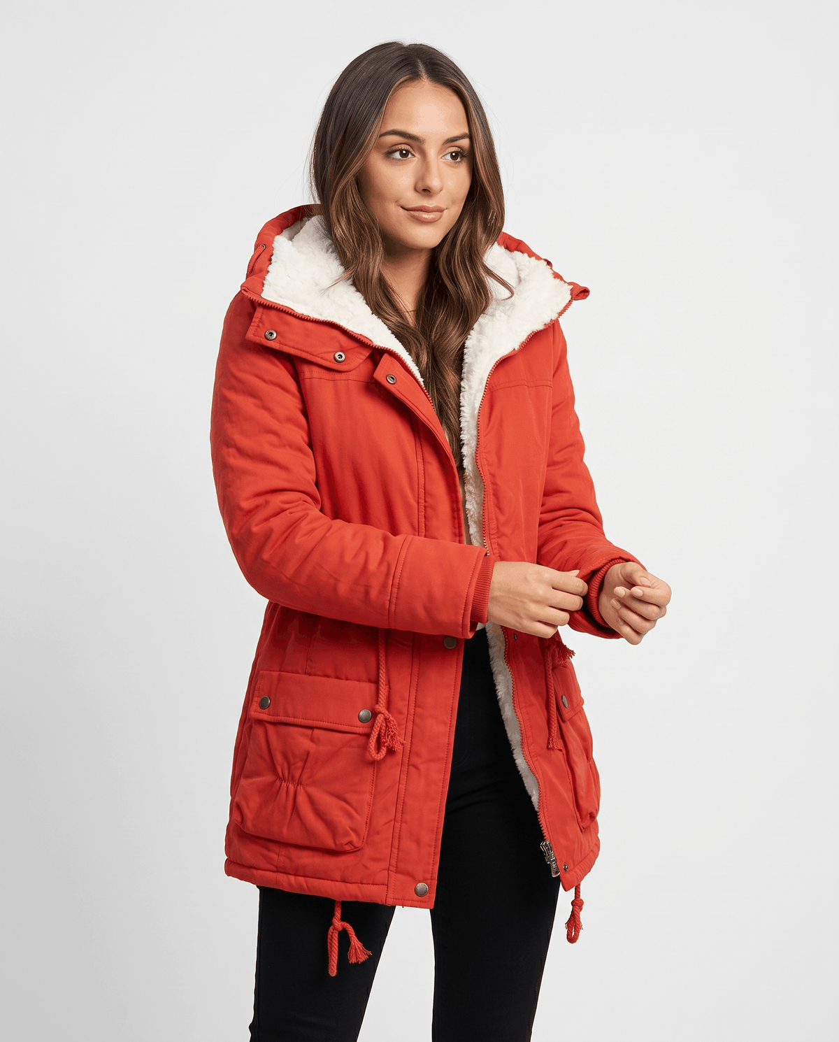 A woman wearing a red mid-length parka jacket with plush lining, a hood, and adjustable waist