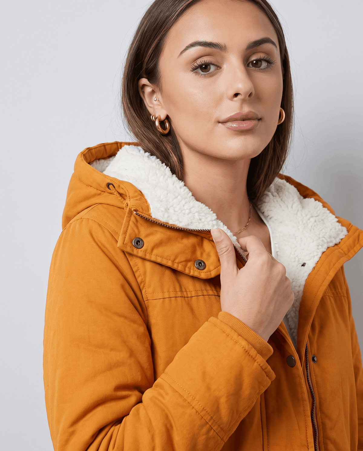 Close-up of a woman wearing a mustard yellow parka jacket, showing the plush-lined hood, collar, and adjustable waist