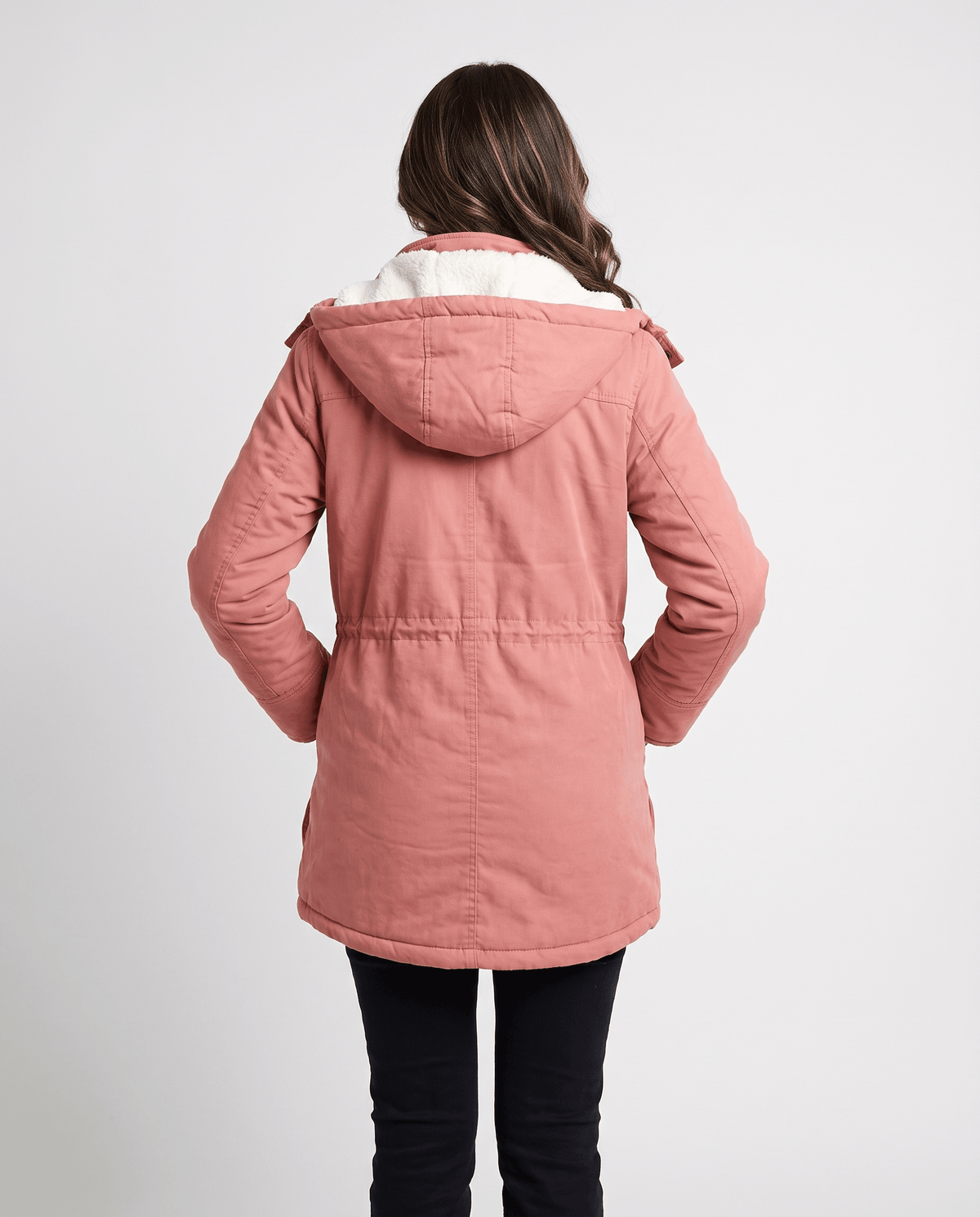A woman wearing a pink mid-length parka jacket with plush lining, a hood, and adjustable waist, shown from the back