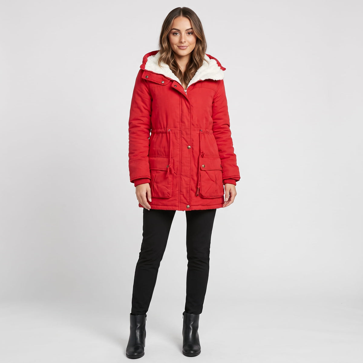 A woman wearing a red mid-length parka jacket with plush lining, a hood, and an adjustable waist