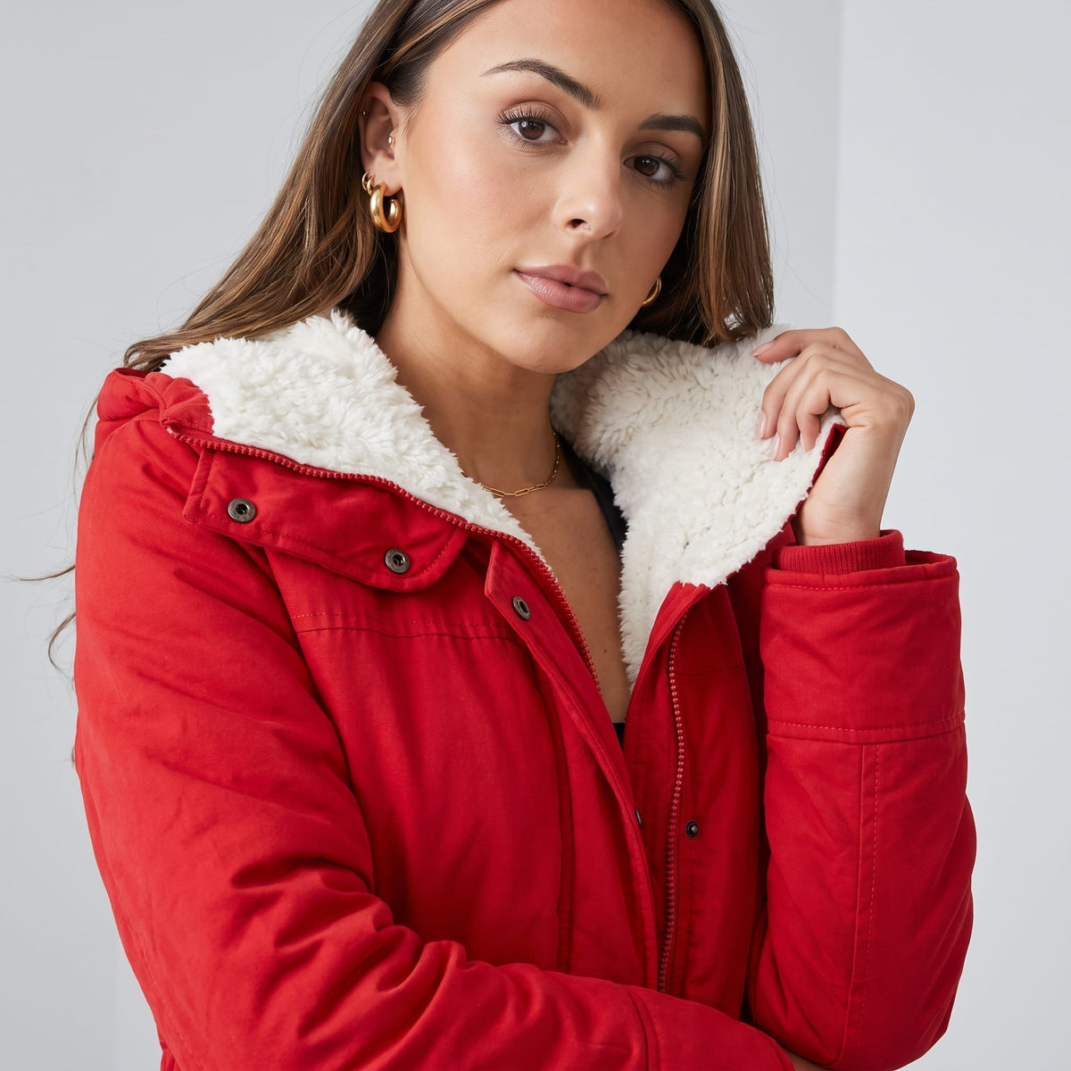 Close-up of a woman wearing a red parka jacket, showing the plush-lined hood and adjustable waist detail