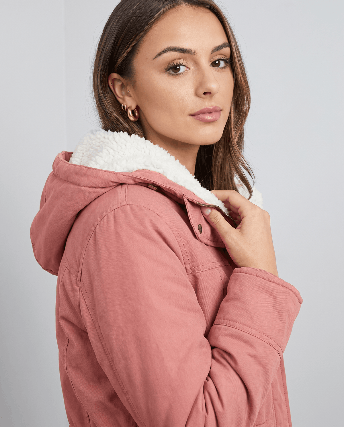 Close-up of a woman wearing a pink parka jacket, showing the plush-lined hood and adjustable waist detail