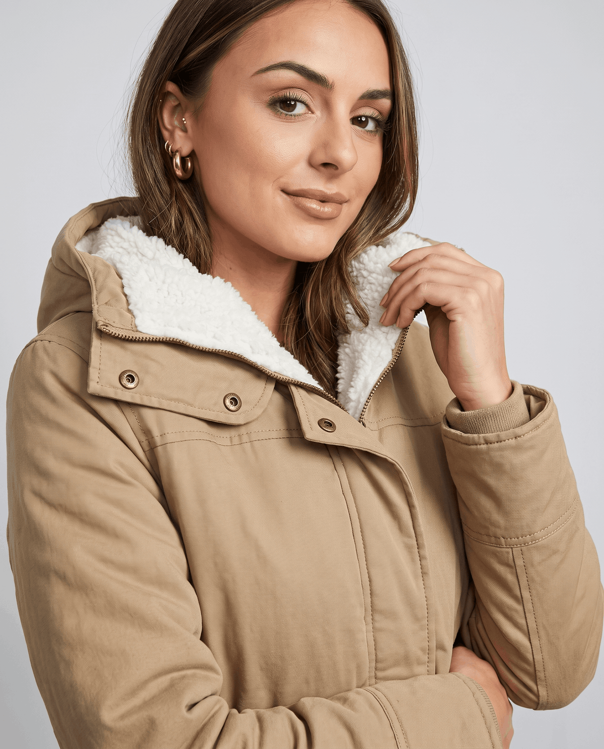 Close-up of a woman wearing a beige parka jacket, showing the plush-lined hood, collar, and adjustable waist