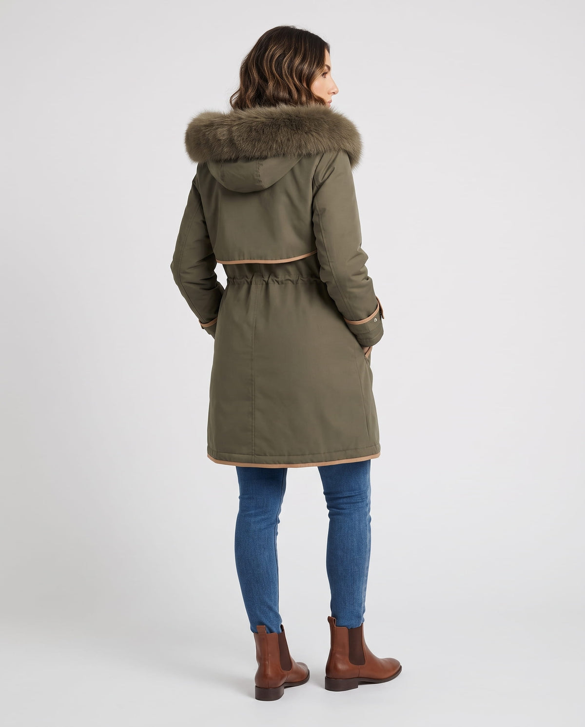 A woman wearing an olive green winter parka with a plush fur-trimmed hood and adjustable waist, shown from the back