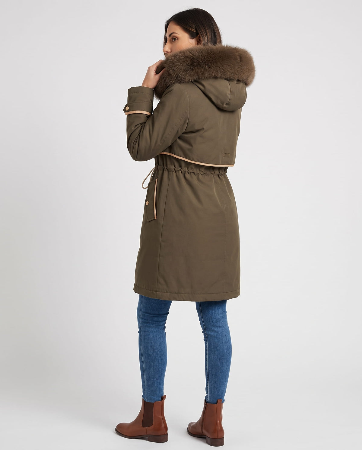 A woman wearing a brown winter parka with a plush fur-trimmed hood and adjustable waist, shown from the back