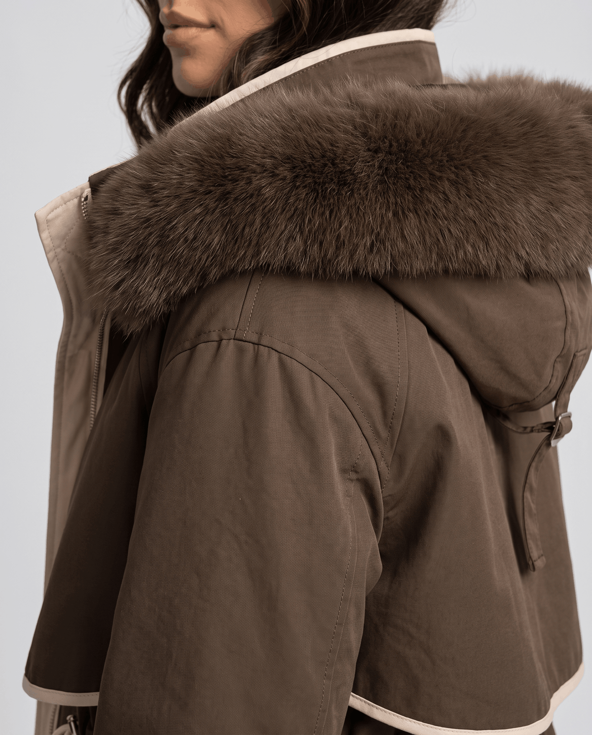 Close-up of a brown winter parka showing the plush fur-trimmed hood and adjustable waist detail