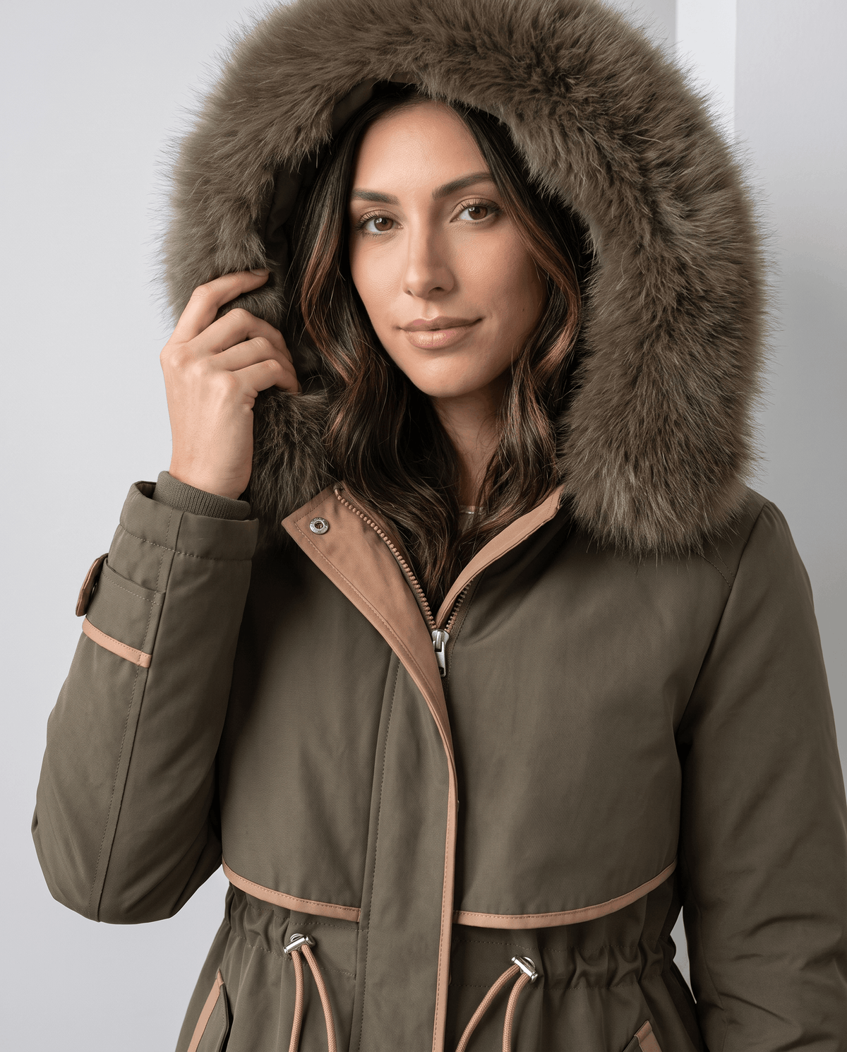 Close-up of a woman wearing an olive green winter parka, showing the plush fur-trimmed hood and adjustable waist