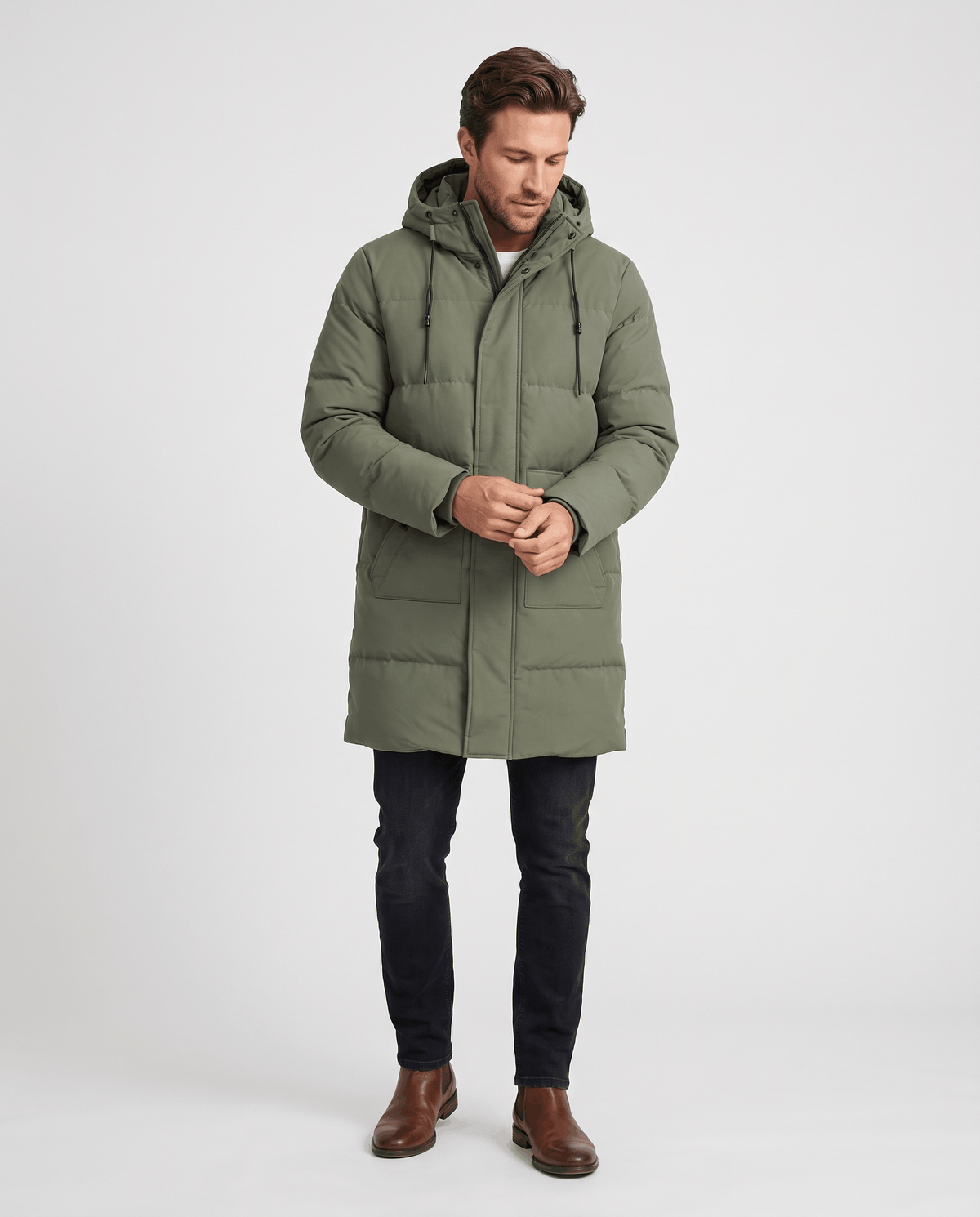 A man wearing an olive green hooded puffer parka jacket with a longline fit and insulated design