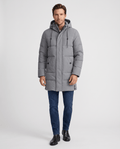A man wearing a gray hooded puffer parka jacket with a longline fit, front zip closure, and insulated design