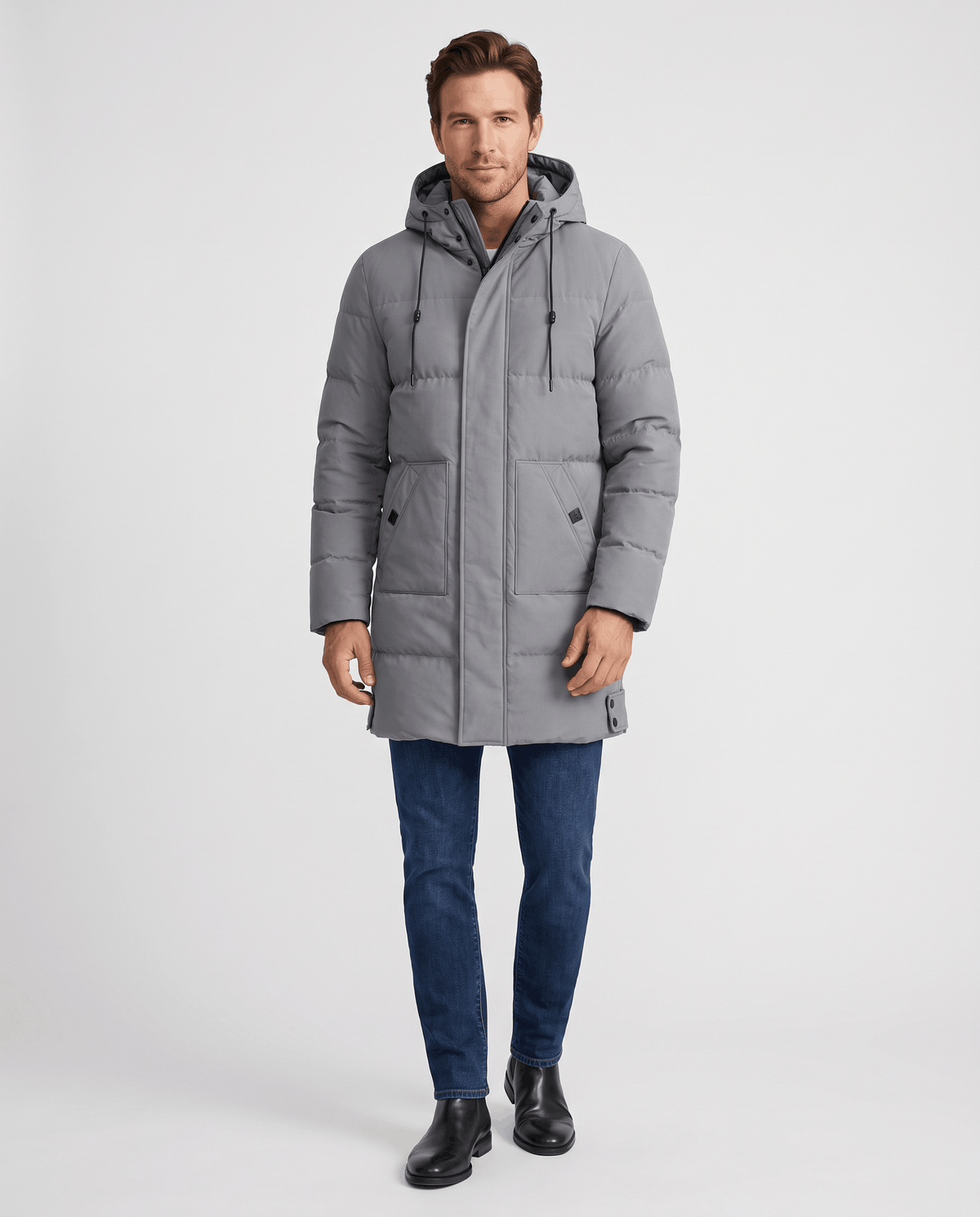 A man wearing a gray hooded puffer parka jacket with a longline fit, front zip closure, and insulated design