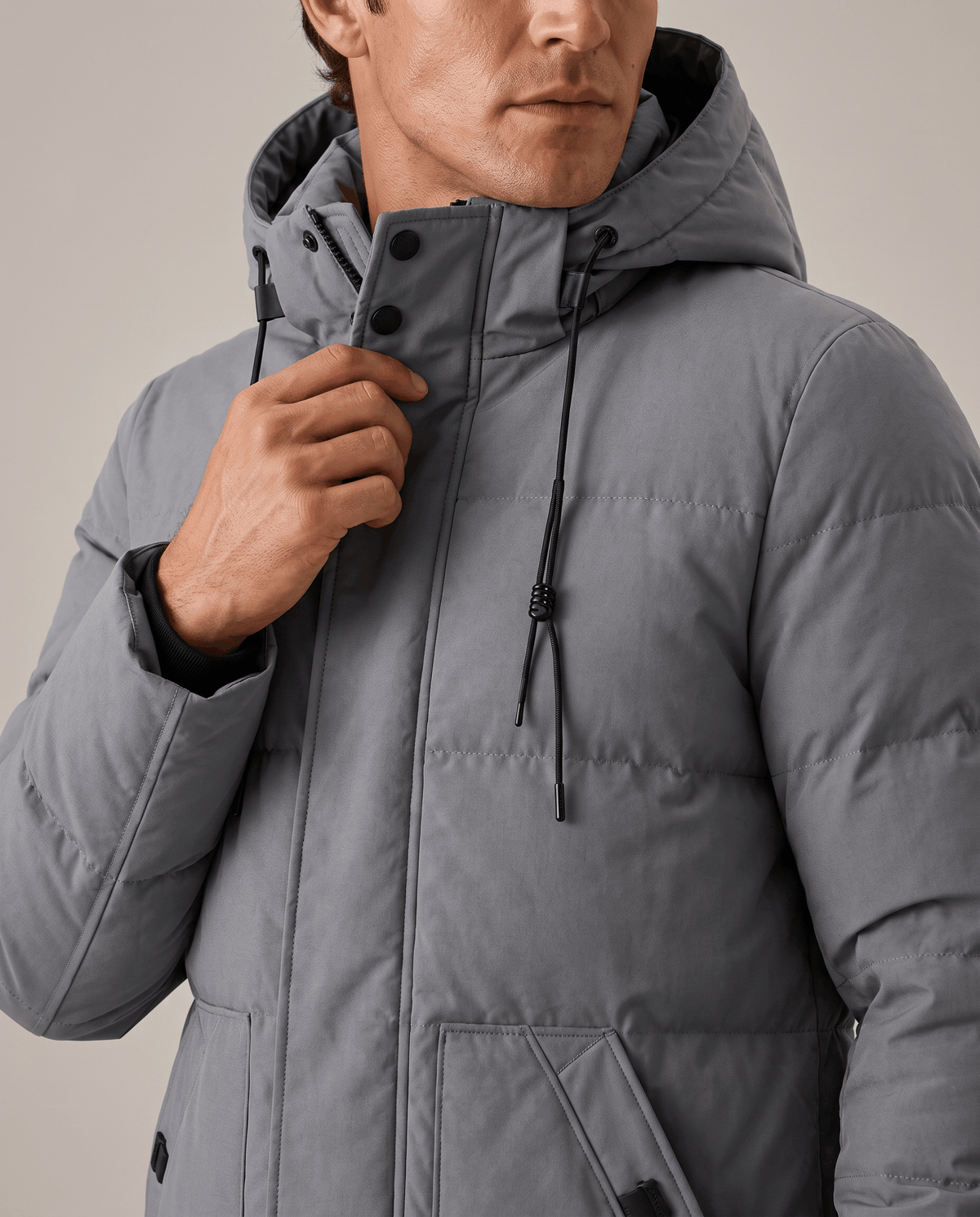 Close-up of a man wearing a gray hooded puffer parka jacket, showing the insulated quilting and hood detail