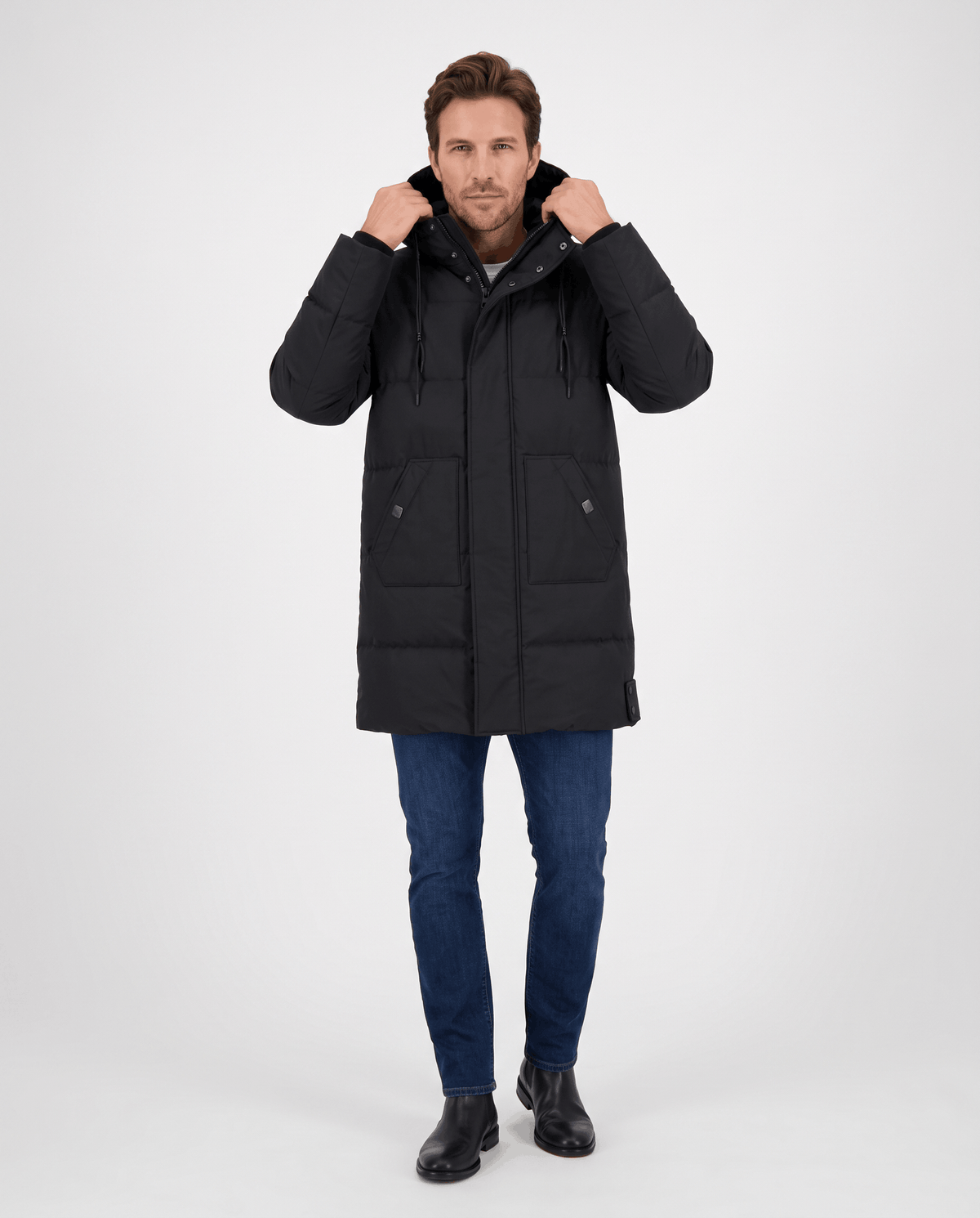 A man wearing a black hooded puffer parka jacket with a longline fit, adjusting the hood