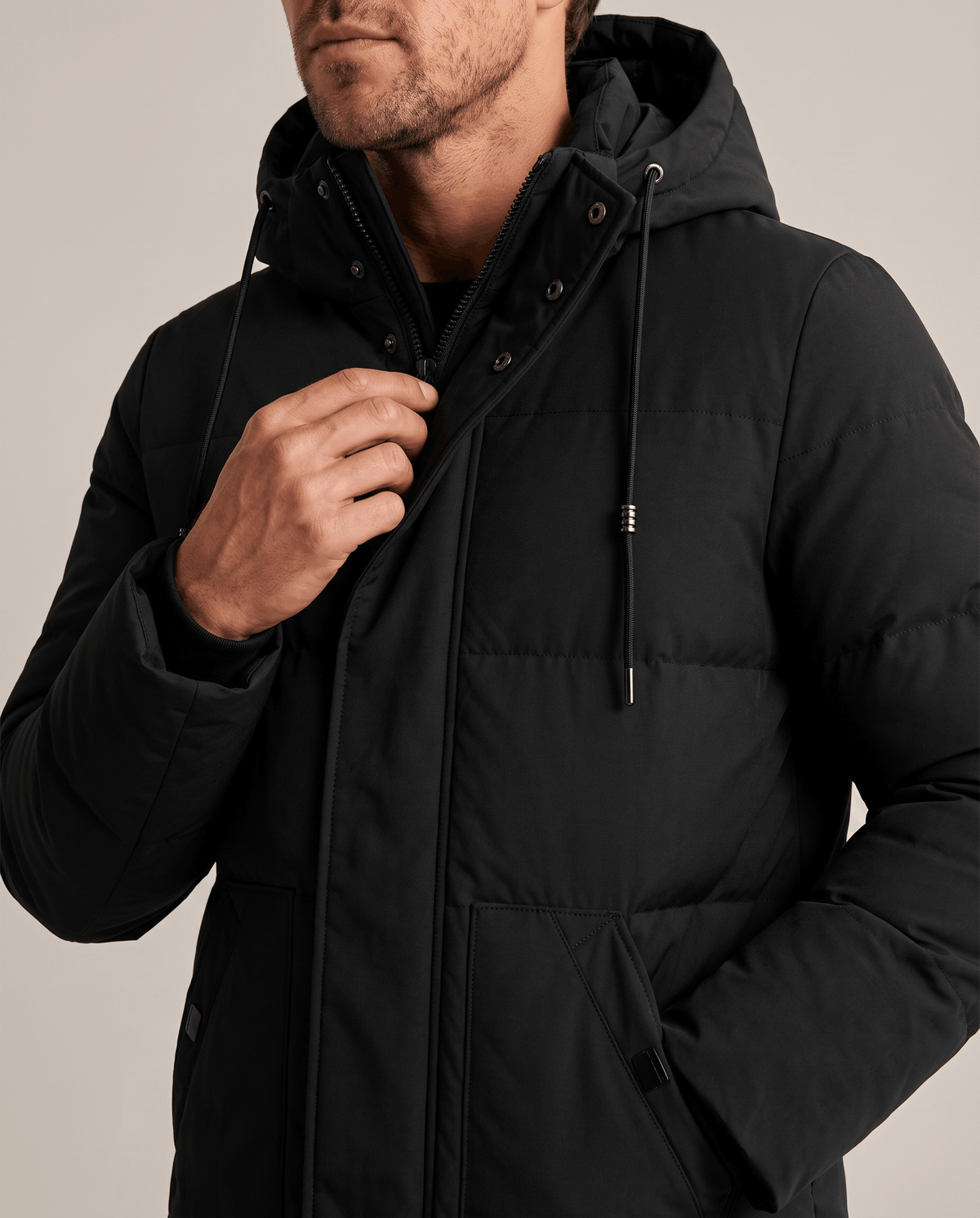 Close-up of a man wearing a black hooded puffer parka jacket, showing the insulated quilting and hood detail