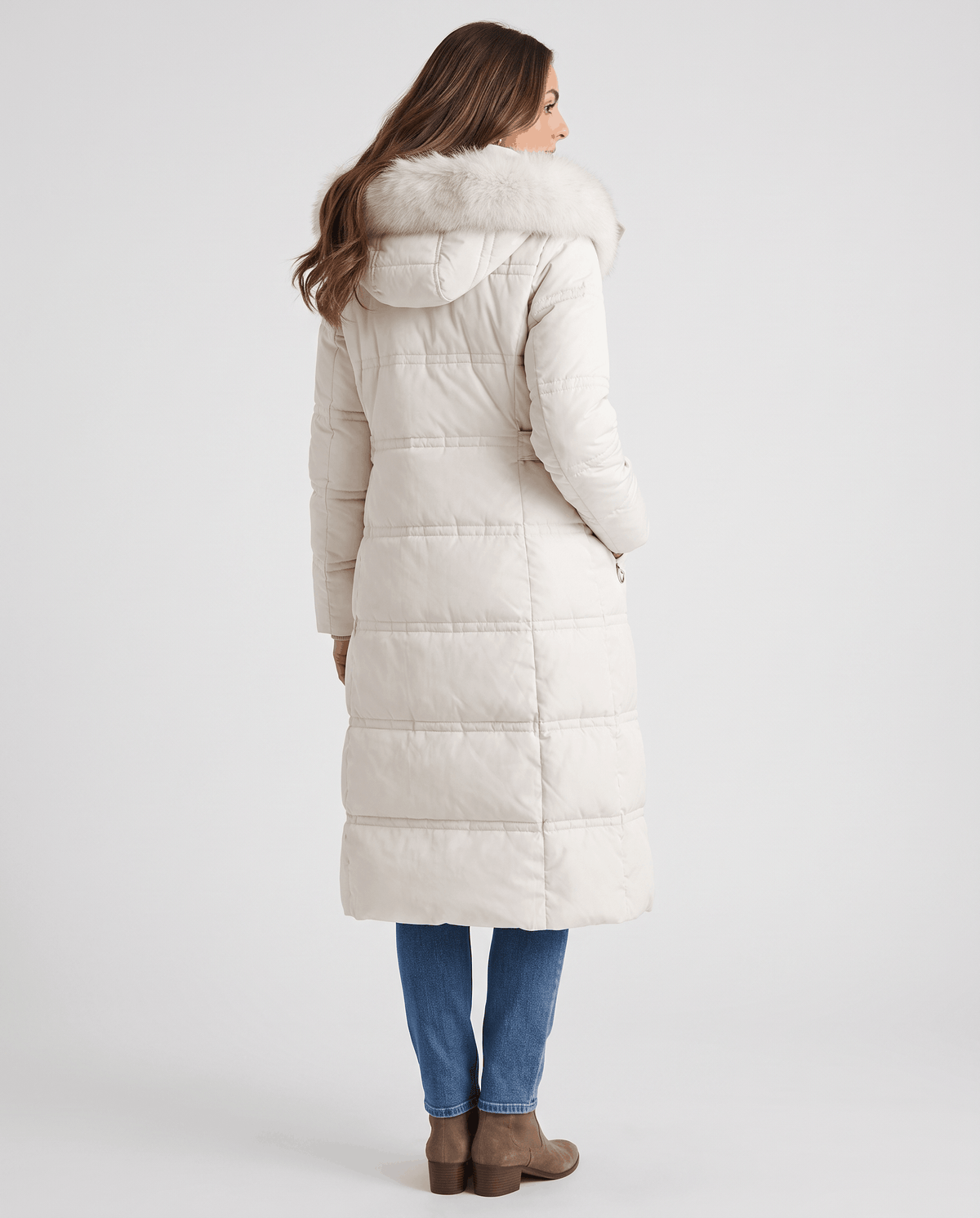 A woman wearing a white quilted winter parka with a longline puffer design and plush fur-trimmed hood, shown from the back