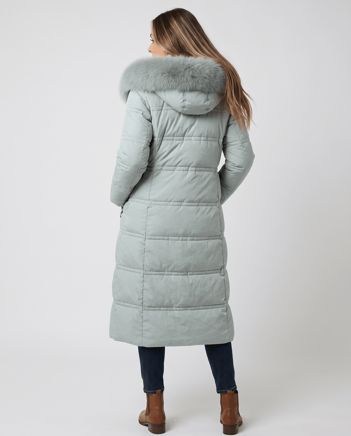 A woman wearing a light blue longline quilted winter parka with a plush fur-trimmed hood, shown from the back