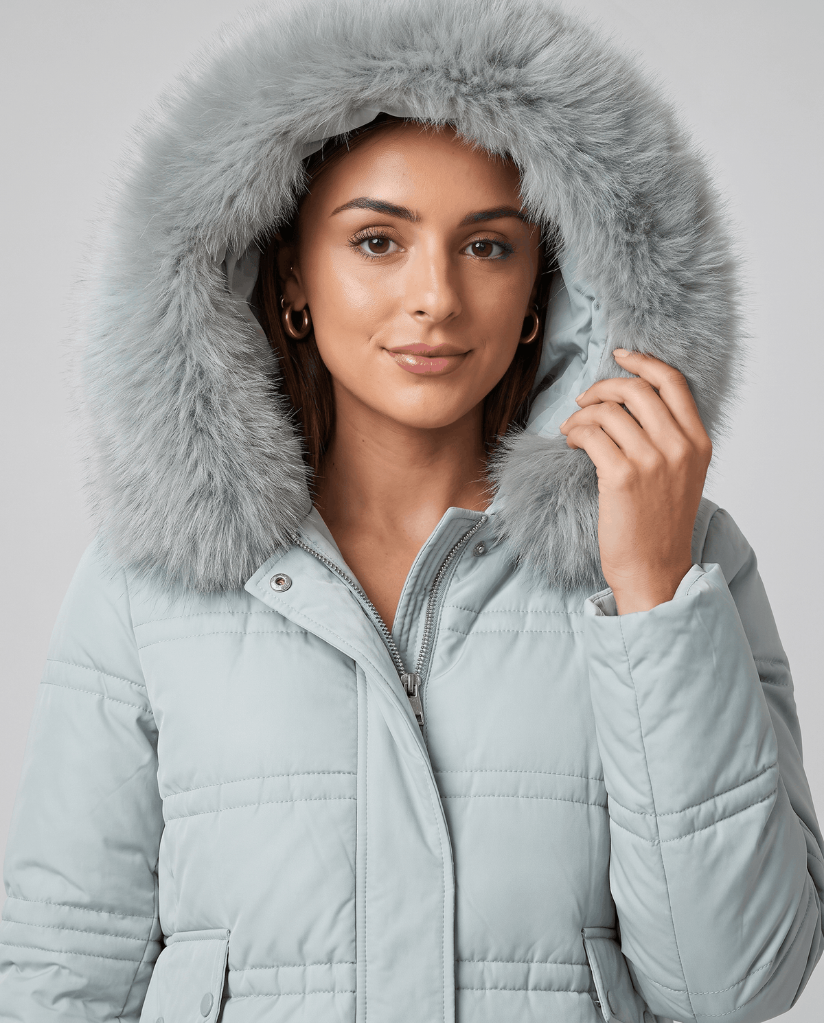 Close-up of a woman wearing a light blue quilted winter parka, showing the plush fur-trimmed hood