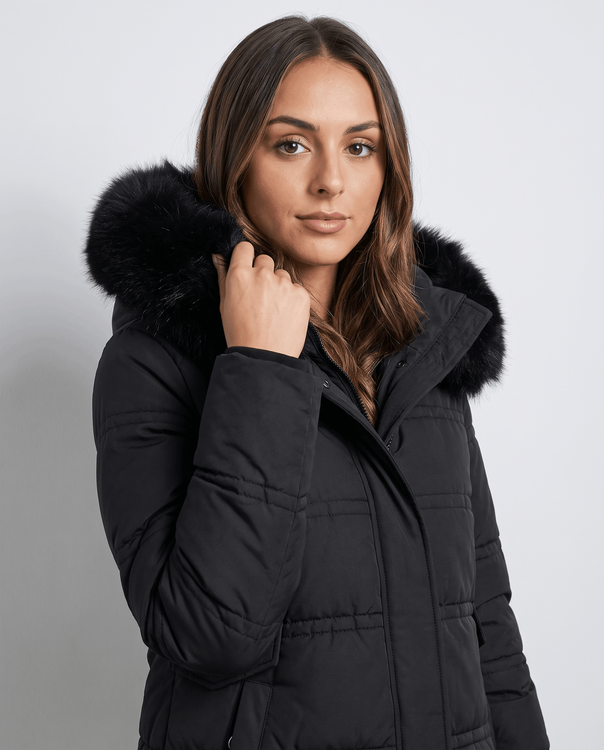 A woman wearing a black longline quilted winter parka with a plush fur-trimmed hood, front view
