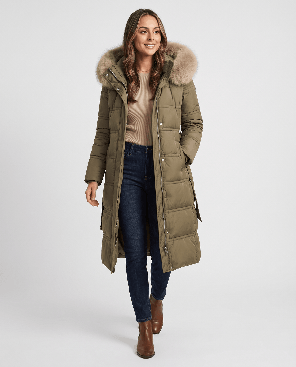 A woman wearing an olive green longline quilted winter parka with a plush fur-trimmed hood, walking outdoors