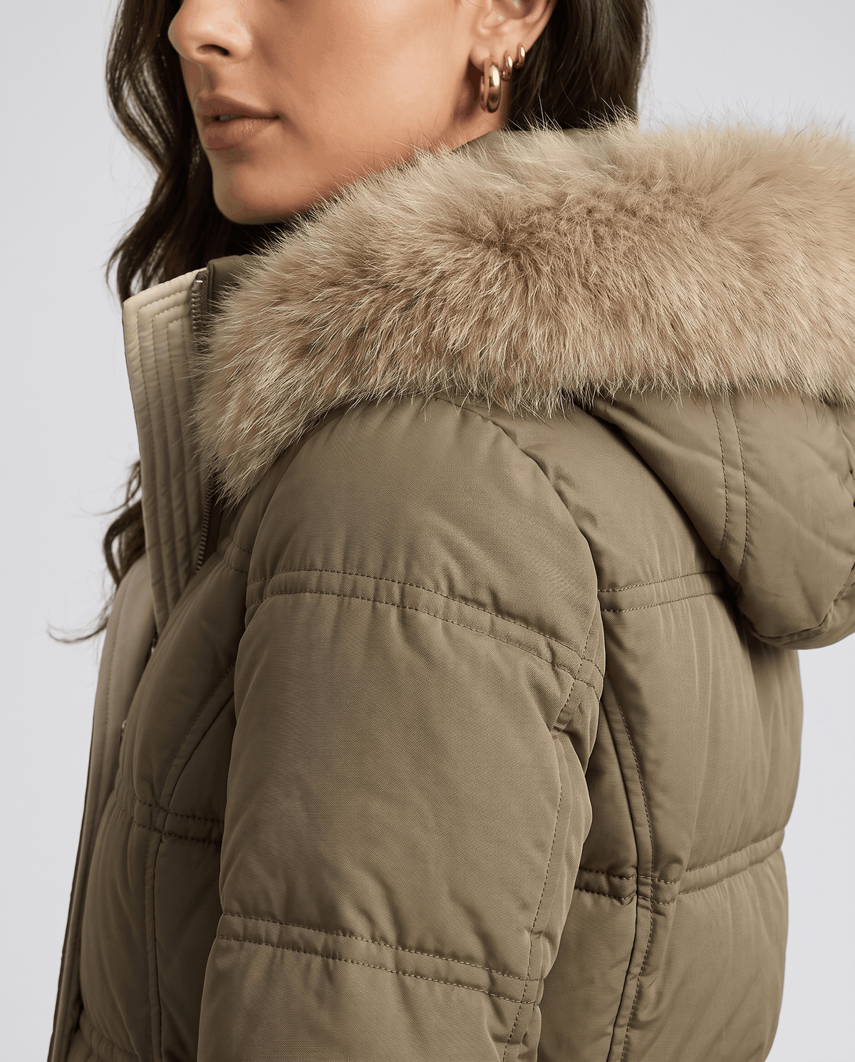 Close-up of a woman wearing an olive green quilted winter parka, showing the plush fur-trimmed hood and collar