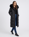 A woman wearing a black quilted winter parka with a longline puffer design and plush fur-trimmed hood