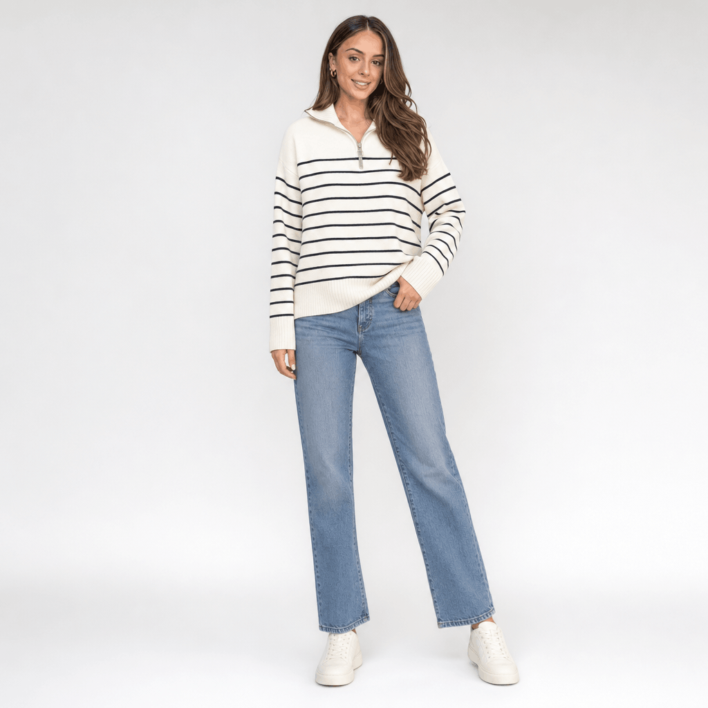 Full-body view of a female model wearing the cream and black striped quarter-zip sweater with blue jeans.
