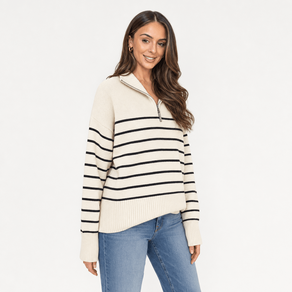 Female model wearing a cream quarter-zip sweater with thin black horizontal stripes, paired with blue jeans.