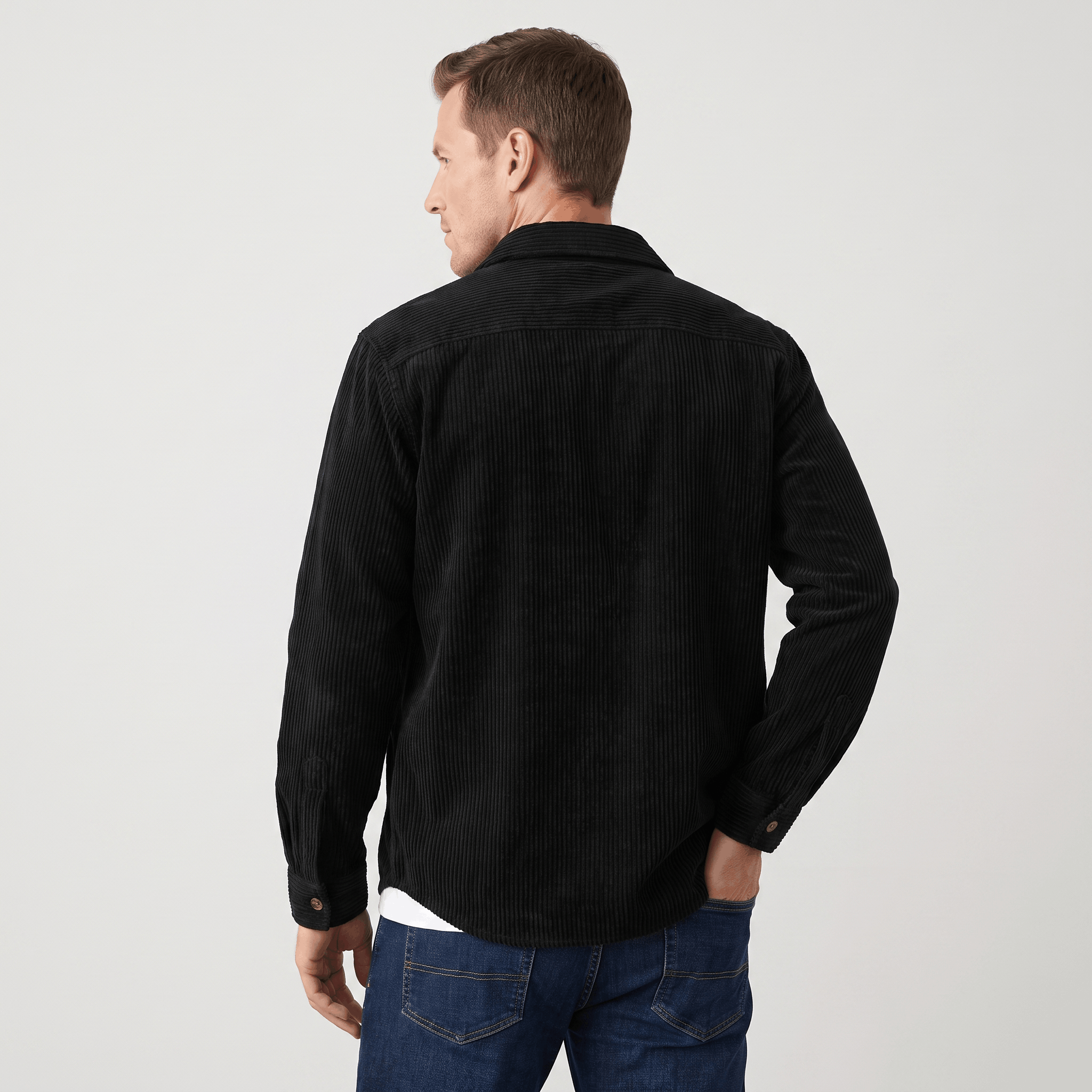 Black wide wale corduroy overshirt in a relaxed fit with a structured collar, worn over a white tee and blue jeans.