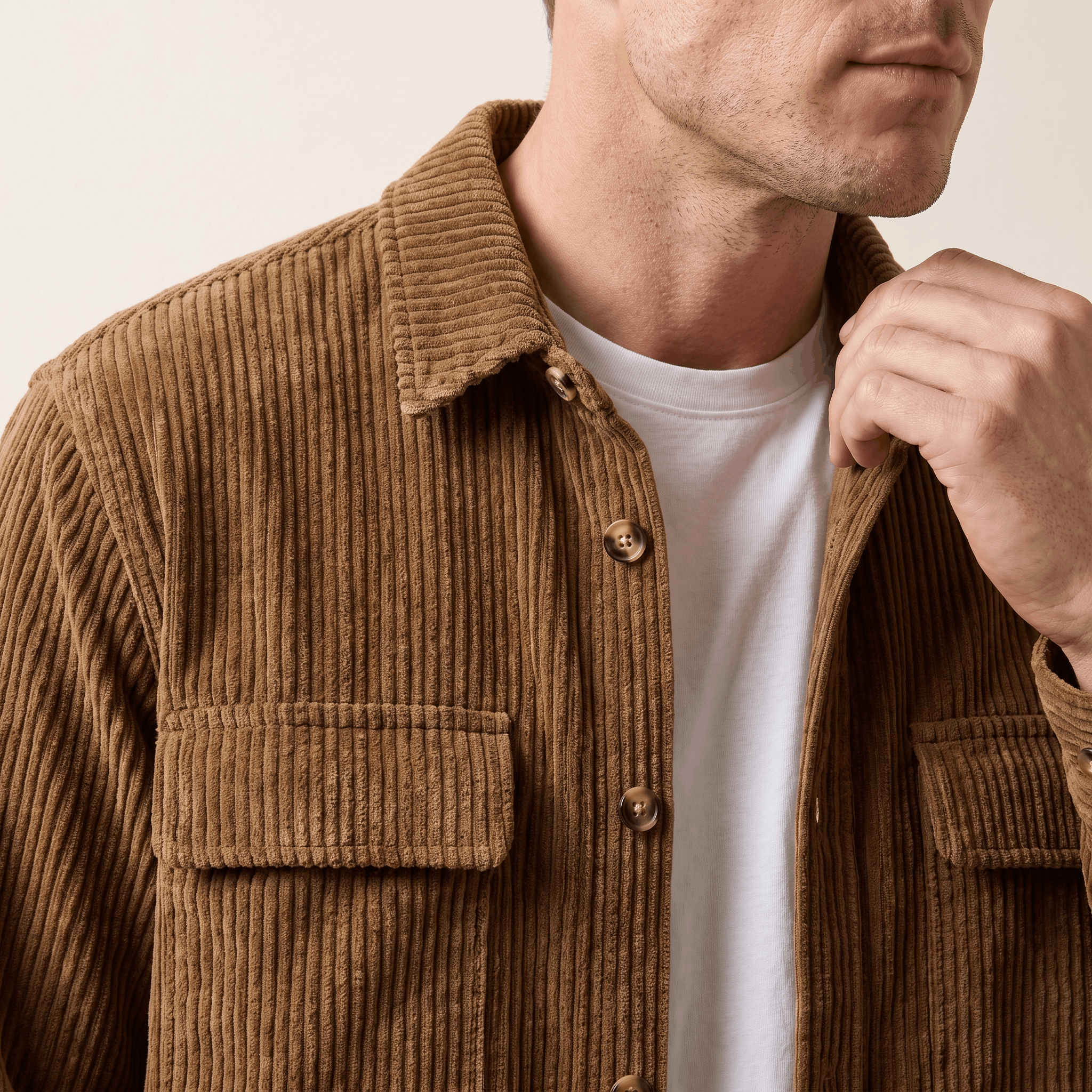 Brown wide wale corduroy overshirt with button-up front and chest flap pockets, worn open over a white crewneck tee.
