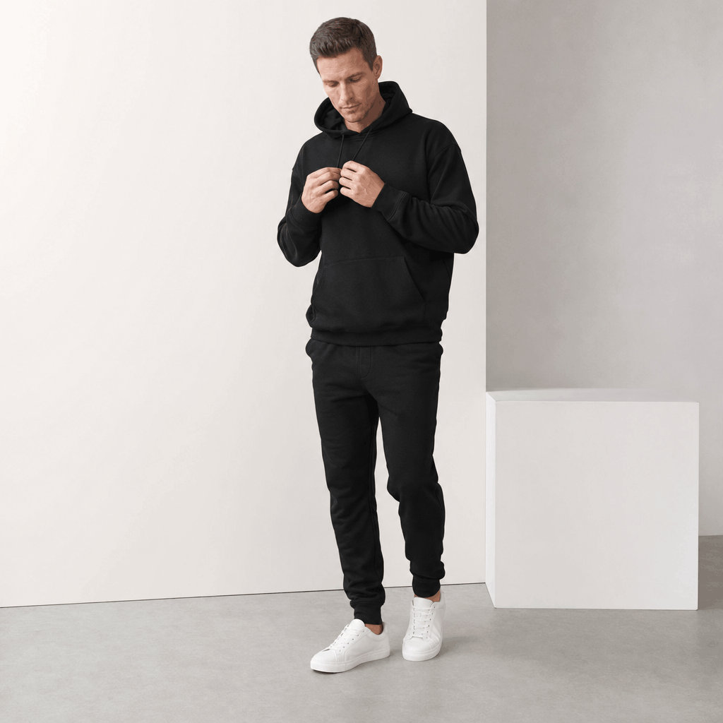 Male model wearing a black pullover hoodie with white sneakers.