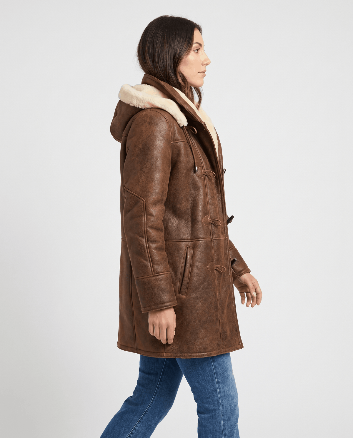 A woman wearing a dark brown shearling duffle coat with a hood, shown in side view