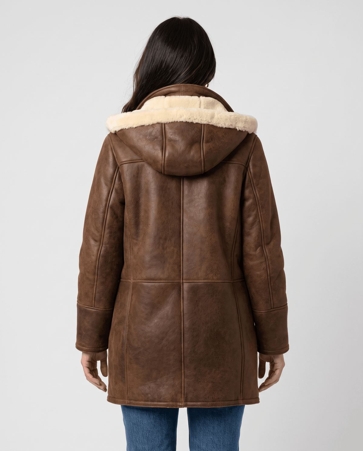 A woman wearing a dark brown shearling duffle coat with a hood and toggle zip closure, shown from the back